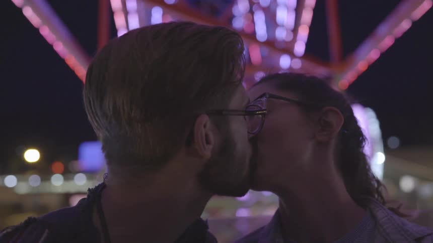 A couple riding a ferris wheel at night are kissing