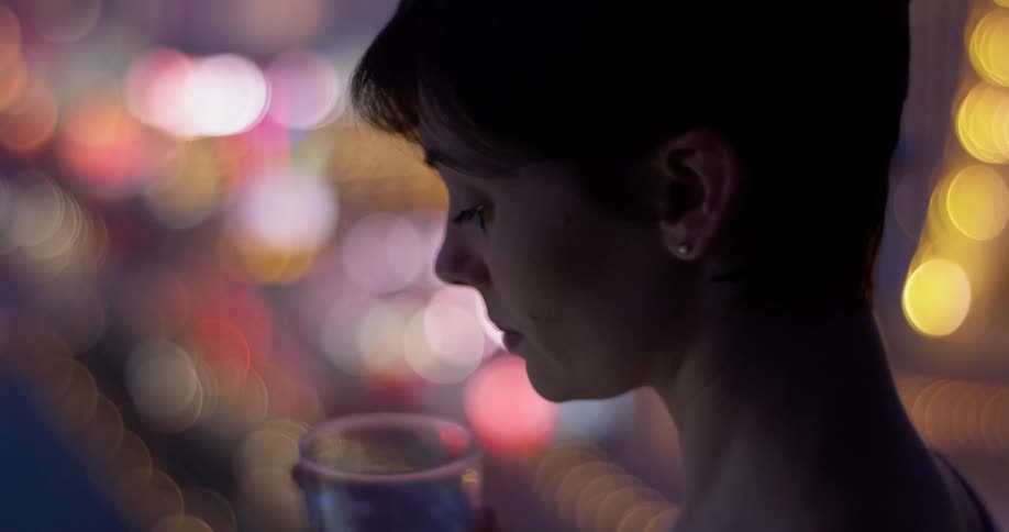 A woman takes a sip of her drink while looking down at city lights