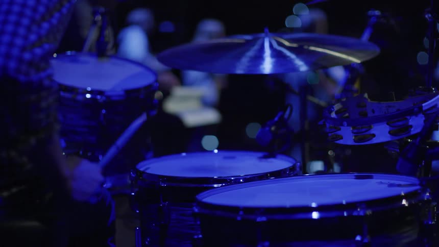 A man slowly plays the drums in the dark