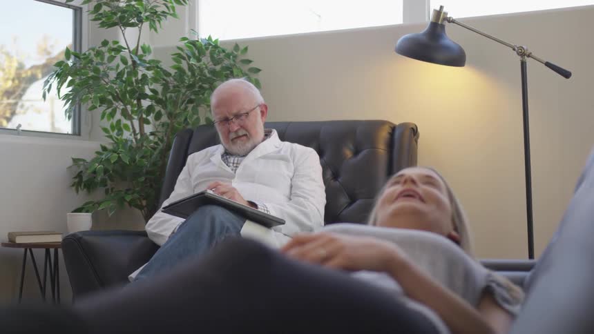 Doctor writes on a clipboard while a woman lays on a couch