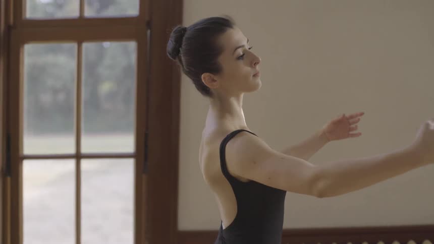 A woman dances down a hallway past windows at day time