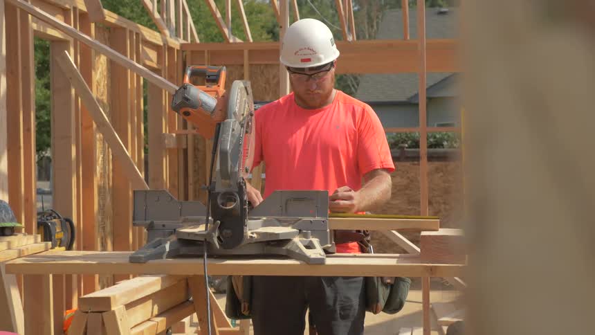 A builder uses a tape measure to mark a piece of lumber before sawing