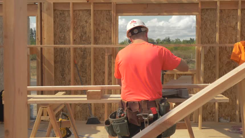 A construction worker is cutting a board outside in daylight