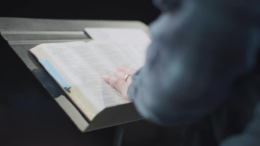 A man reads from a book while standing at a podium