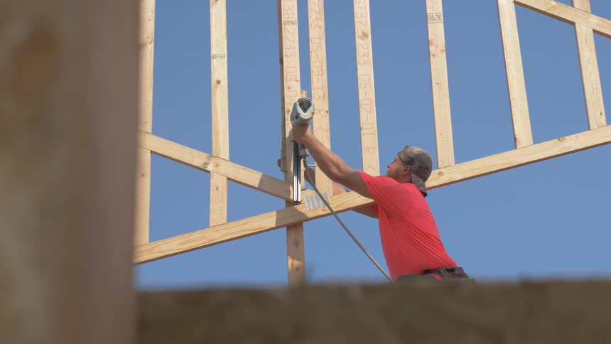 A construction worker is using a nail gun outside on a sunny day