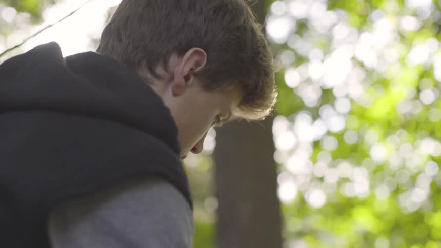 Young man wearing a vest sits in the forest on a sunny day