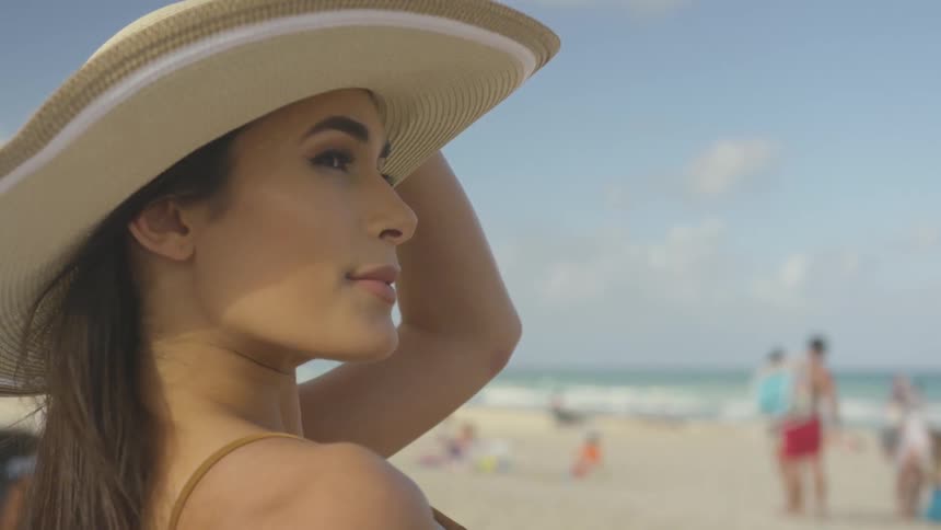 A woman is holding her hat as she lounges on a beach in daylight
