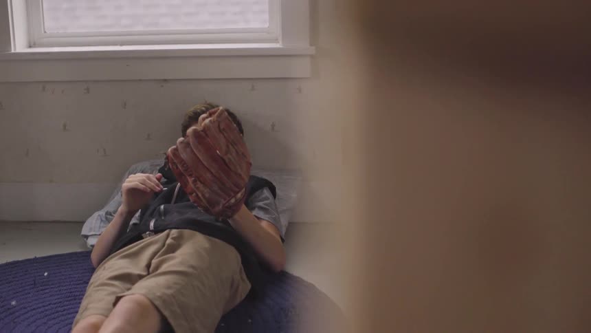 A boy lies on the floor and tosses a ball into his glove