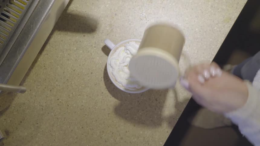 A barista is piping whipped cream onto a coffee inside a sho in daylight