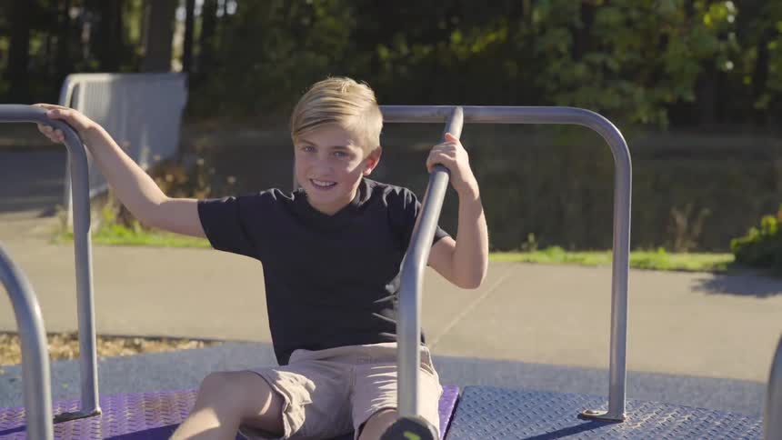 Boy sitting on spinning roundabout park toy on sunny day