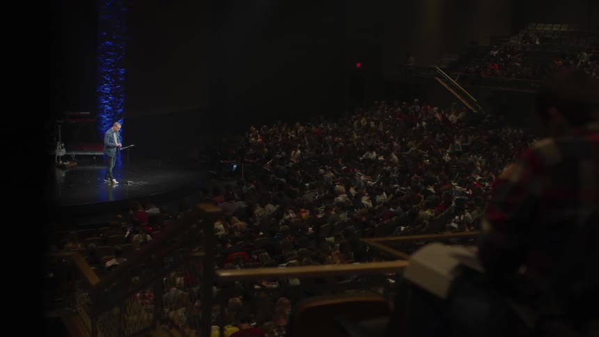 A man speaks on a stage in front of a large audience