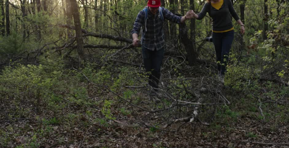 A man and a woman hold hands as they walk through the woods