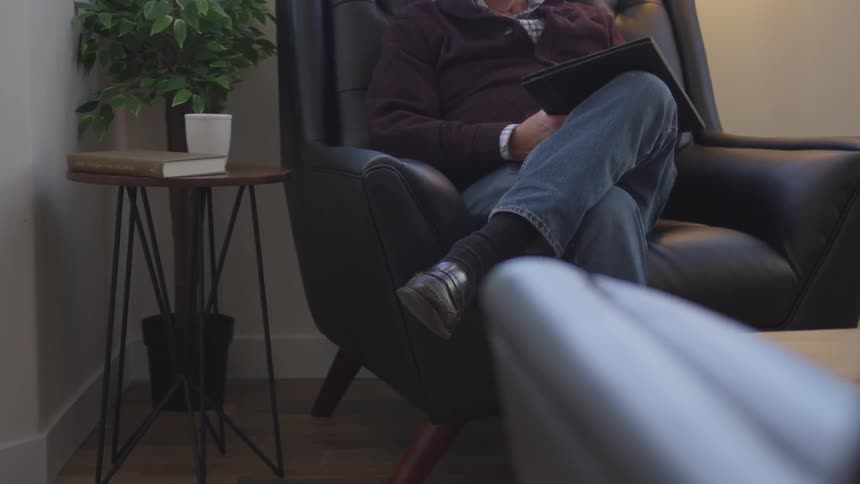 Man sits in a black chair as he holds a tablet
