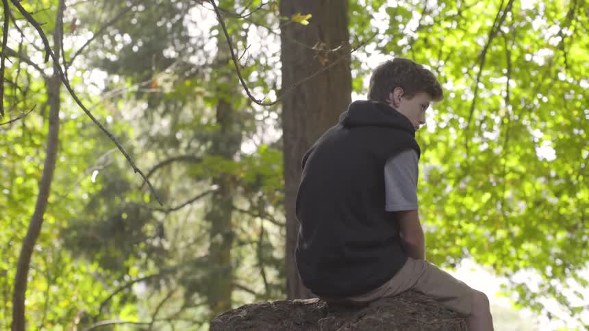 Boy sits outside on a large rock in the woods