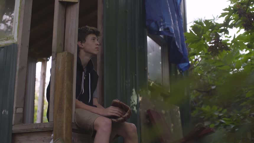 Child holds a baseball mitt and ball and sits in a treehouse