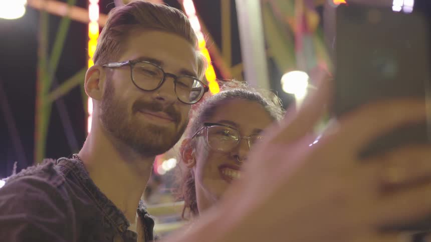 Man and woman taking selfie in front of ferris wheel at fair