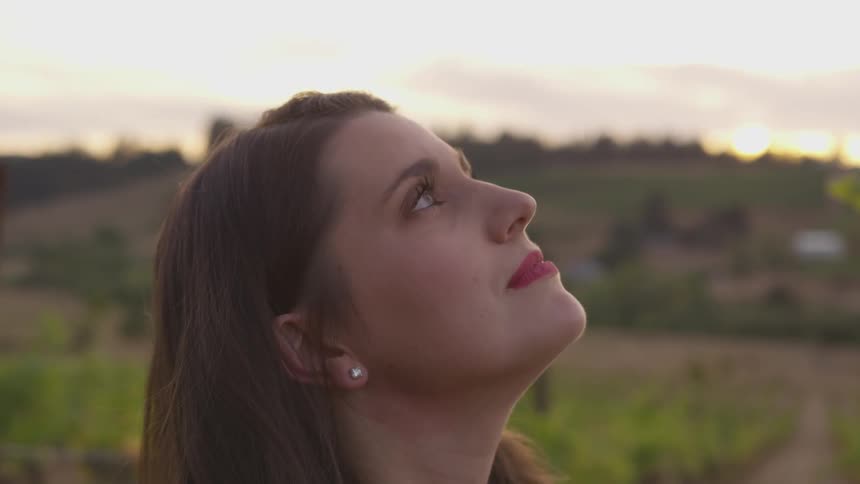 A woman smiles looking up at the sky in the vineyard