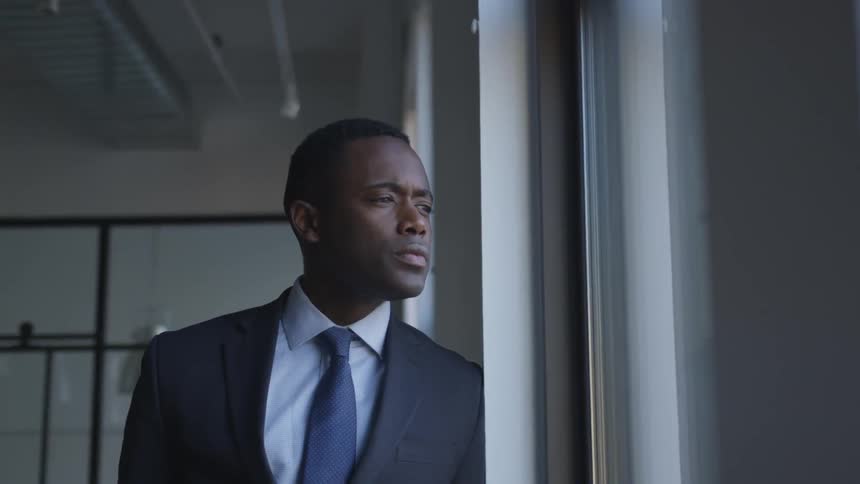 A man leans against the wall looking out the window