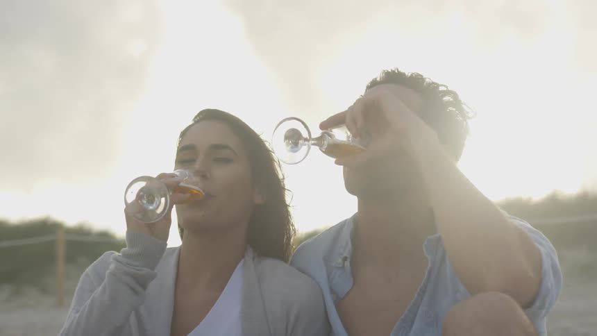 A couple are sitting outside on a beach drinking champagne