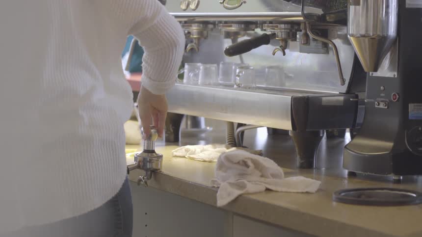 A barista is preparing to make an espresso inside a shop in daylight