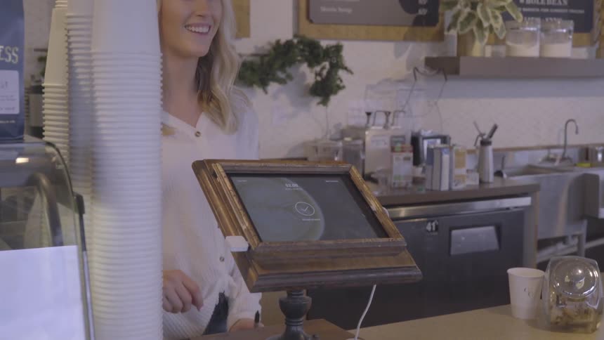 A woman hands a paper over a counter to another then tilts the order screen