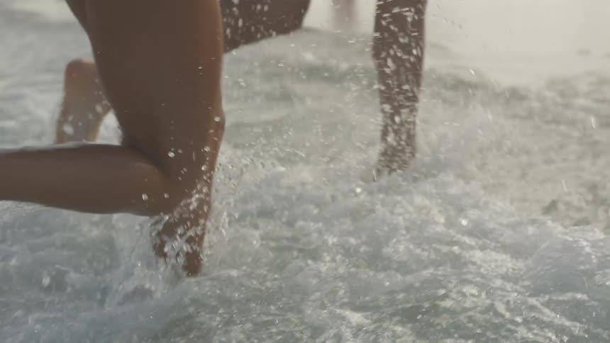 Man and woman run on the beach splashing water