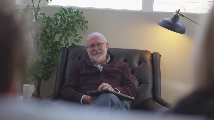 A man smiles while writing in the chair