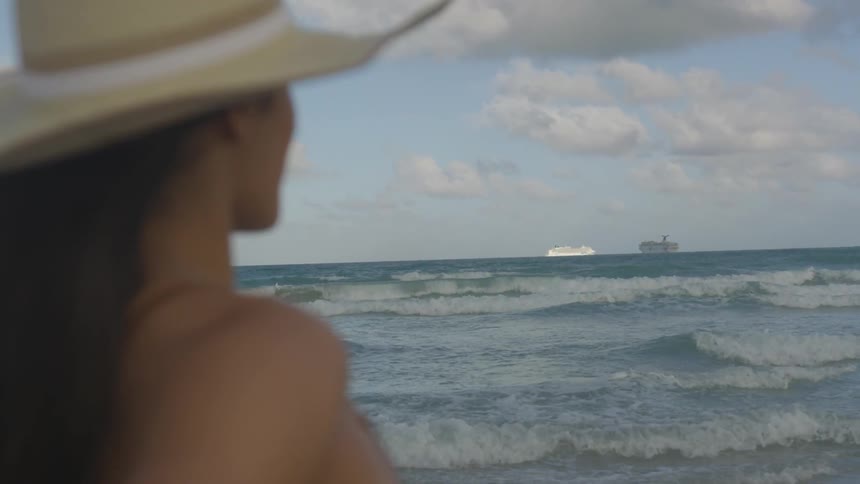 A woman wearing a hat looks out at the waves