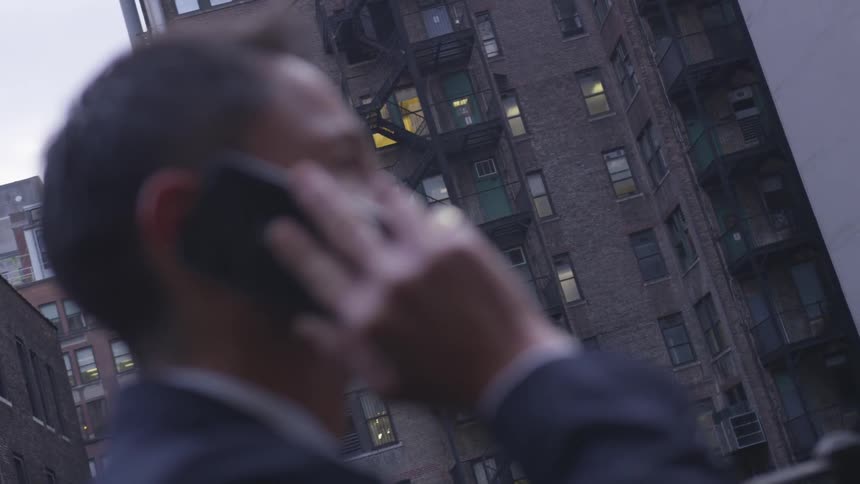 A businessman talks on a phone on a city sidewalk
