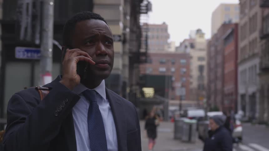 A businessman talks on a phone on a city sidewalk