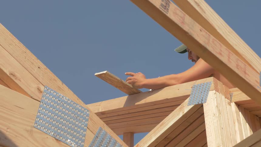Man hammers a piece of wood onto a beam on a structure