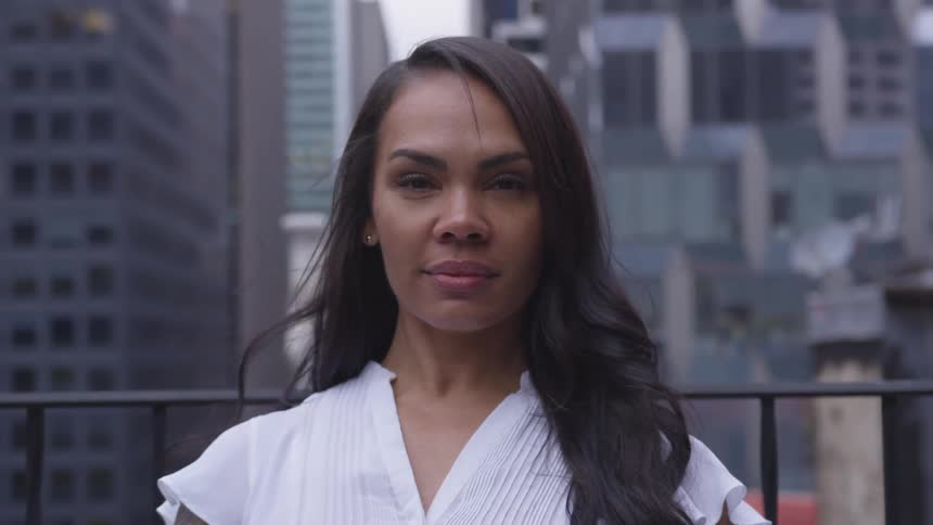 A woman standing on a balcony in a city turns her head and stares