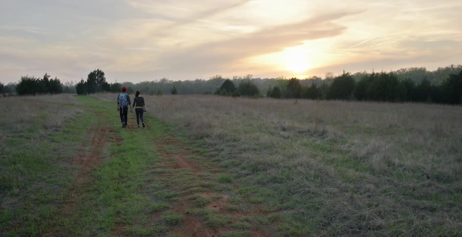 A man and woman walk down a large field at sunset