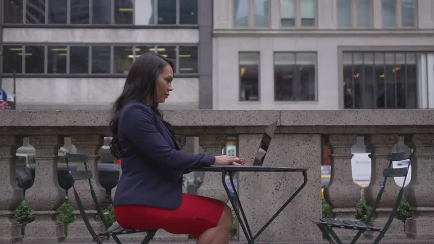 A woman uses a laptop on a city sidewalk