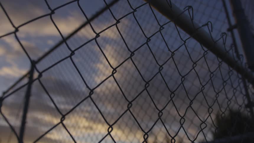 A cloudy sky seen through a chain link fence