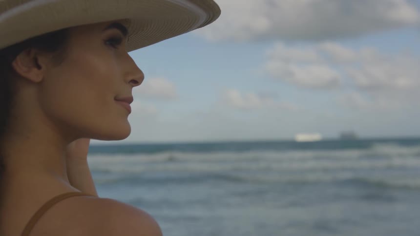 A woman holds her hat on in the windy beach