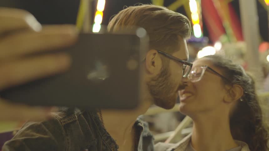 A man and woman kiss as they take a selfie at the carnival