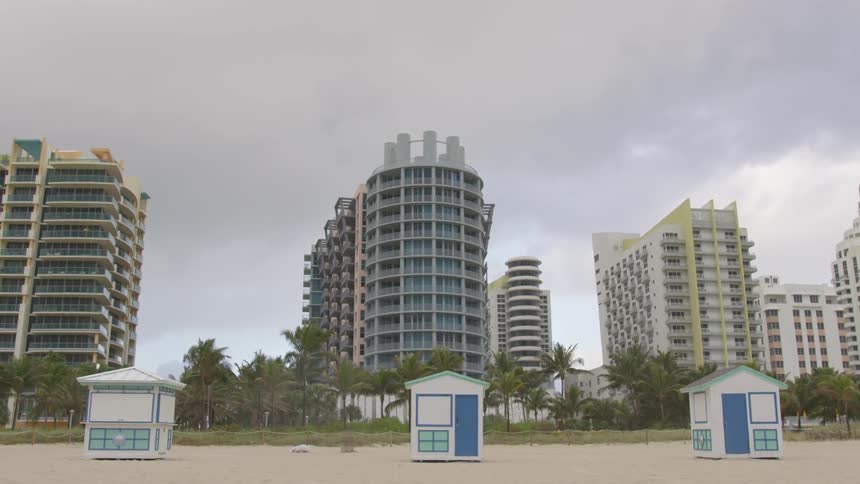 Cabanas on a beach with palm trees and buildings behind them