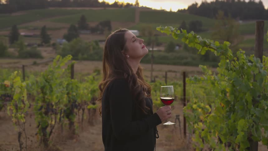 A woman holding a wine glass looks up and smiles in a vineyard