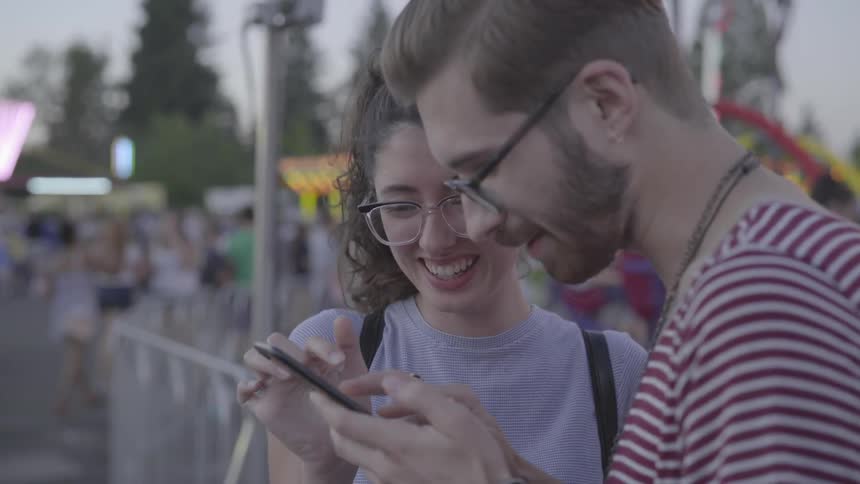 Man and woman are looking at cell phone and smiling at fair