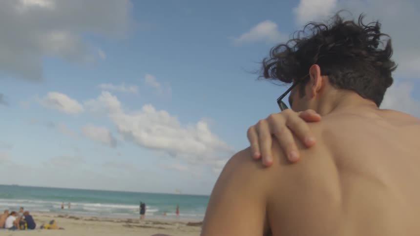 The man rubs his shoulder and arm on the beach