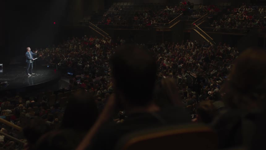 Man stands on stage talking in front of an audience