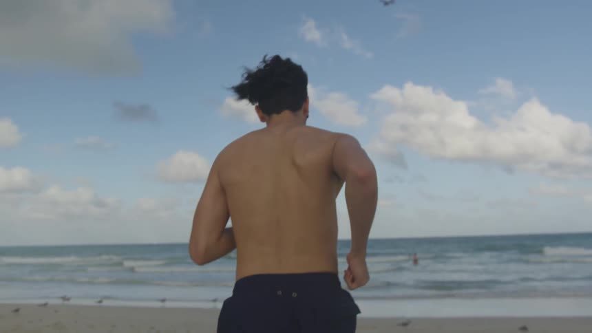Man wearing sunglasses runs on the beach towards the ocean