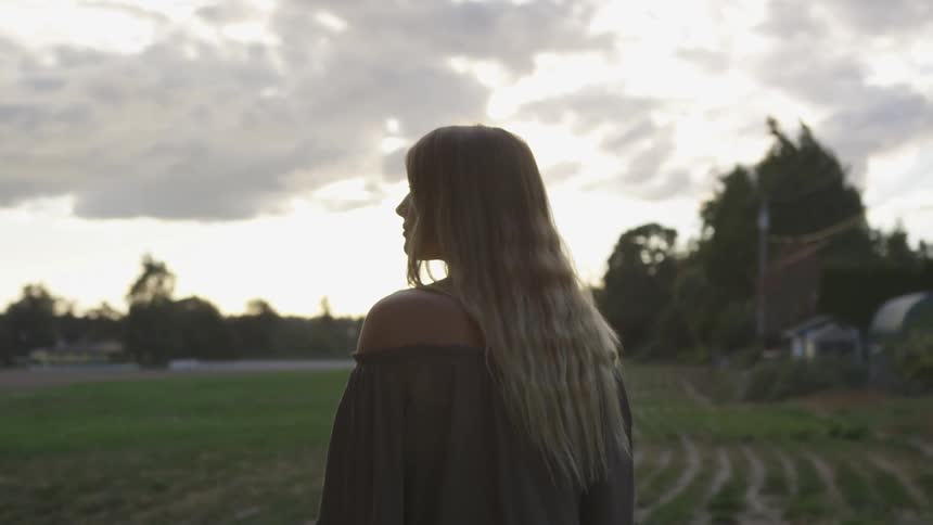 A woman stands on a farm at sunset