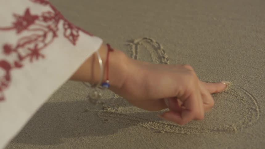 A woman traces a heart shape in the sand