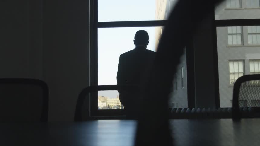 A man wearing a suit looks out an office window