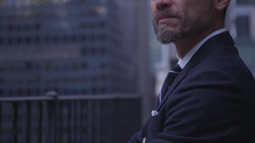 A businessman stands in a city with his arms crossed