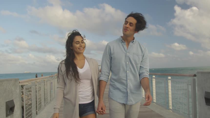 The man and woman walk on the pier holding hands