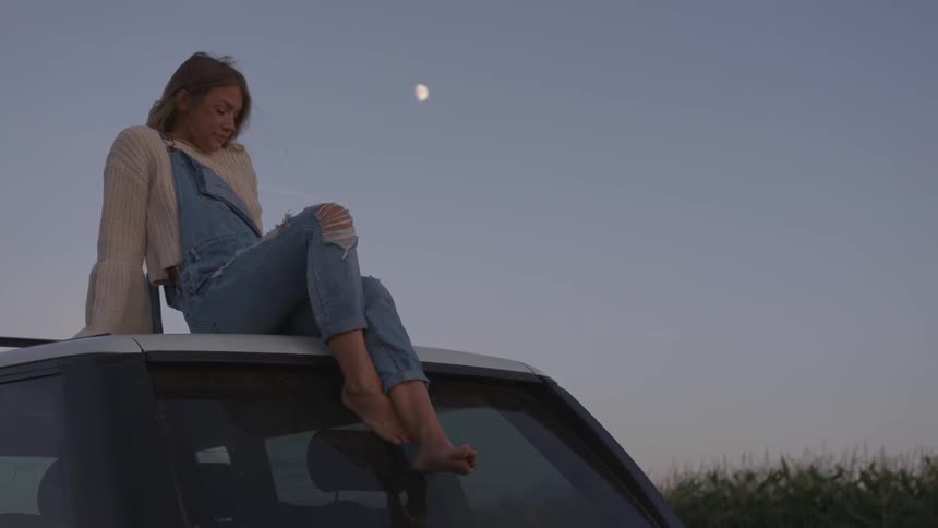 Woman sits on top of a vehicle in the evening