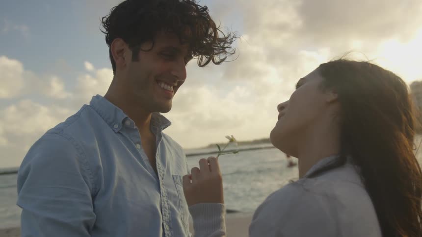 Man hands a woman a small flower as they stand on the beach